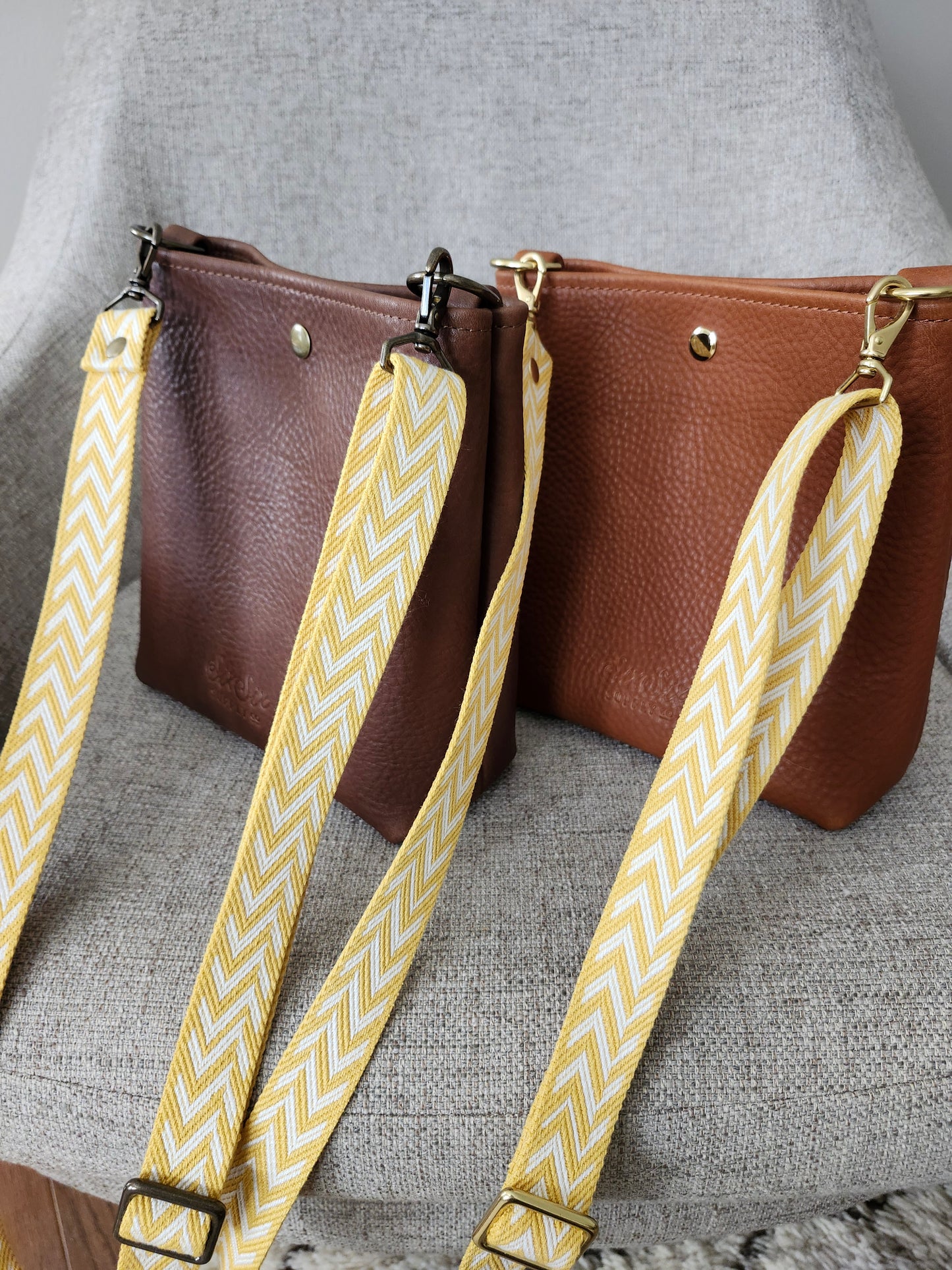 Brown leather handbag with yellow and white patterned strap on a gray surface