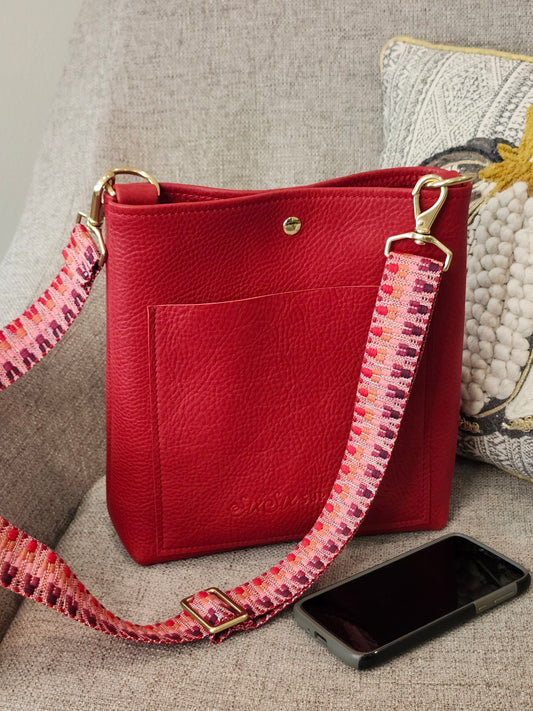 Red handbag with a colorful strap on a textured surface
