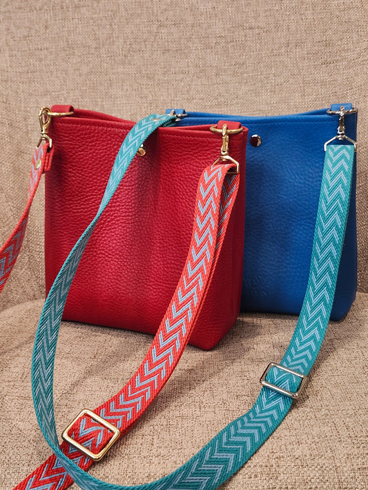 red crossbody with red and blue zigzag webbing strap and blue crossbody with blue zigzag webbing strap.