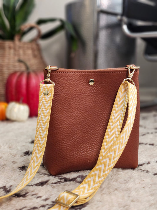 Brown leather handbag with a yellow strap on a textured surface
