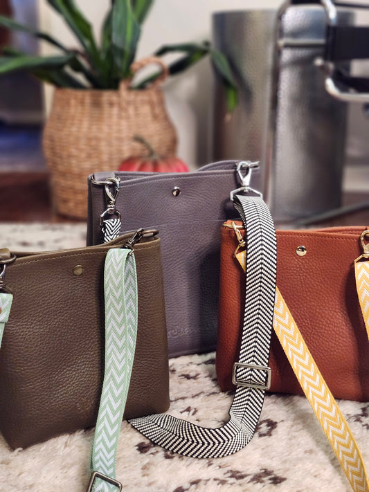 Collection of handbags with colorful straps on a textured surface.