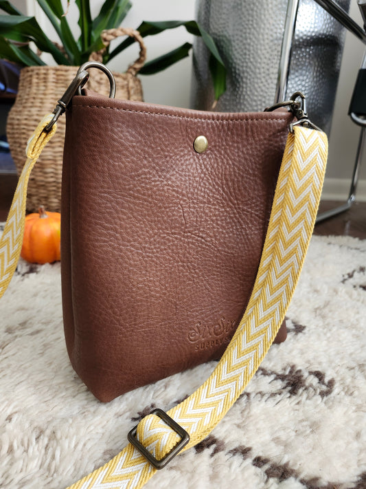 Brown leather bag with a yellow strap on a textured surface