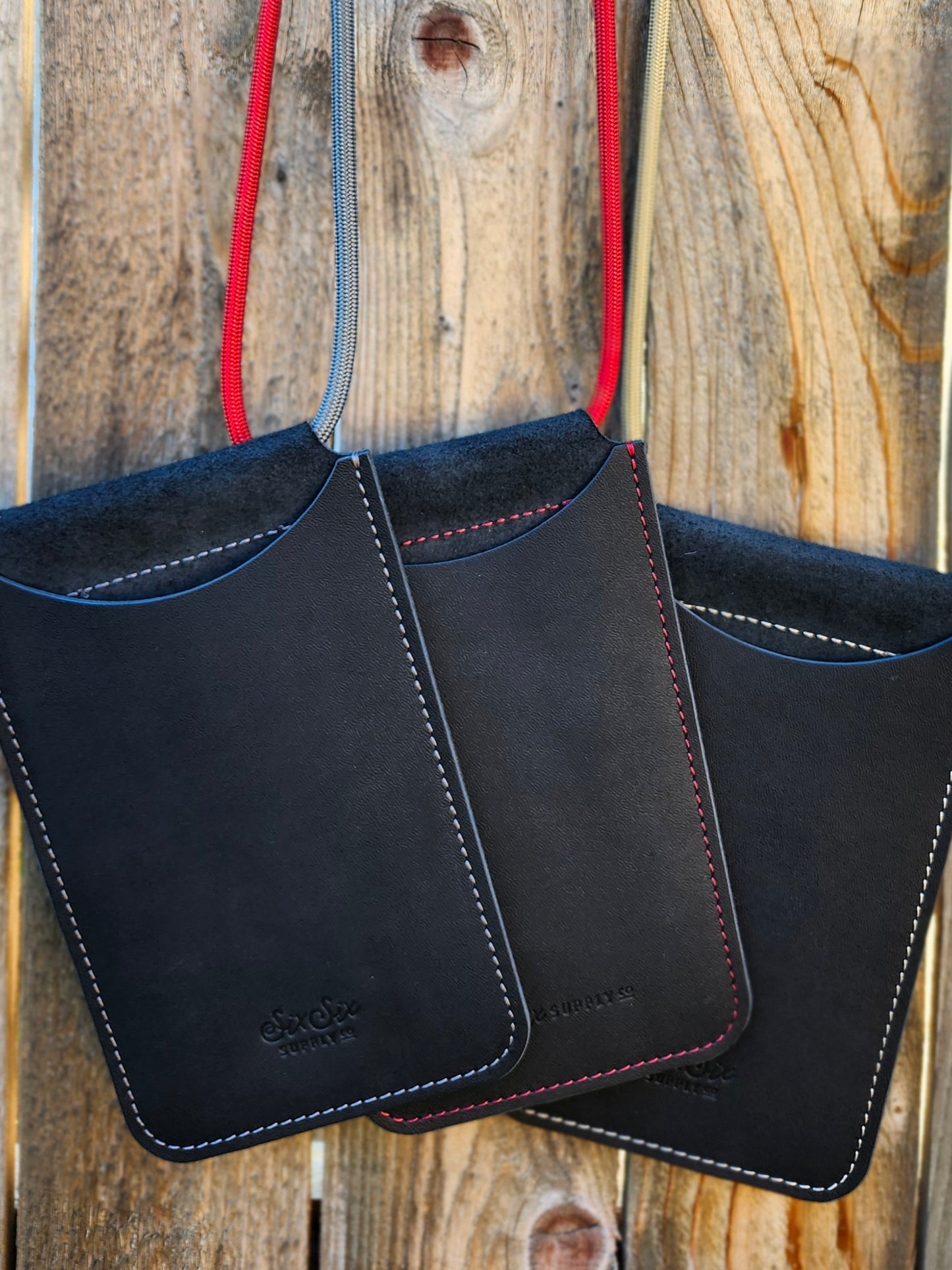 Black leather phone pockets with silver, red and gold stitching on a wooden surface 