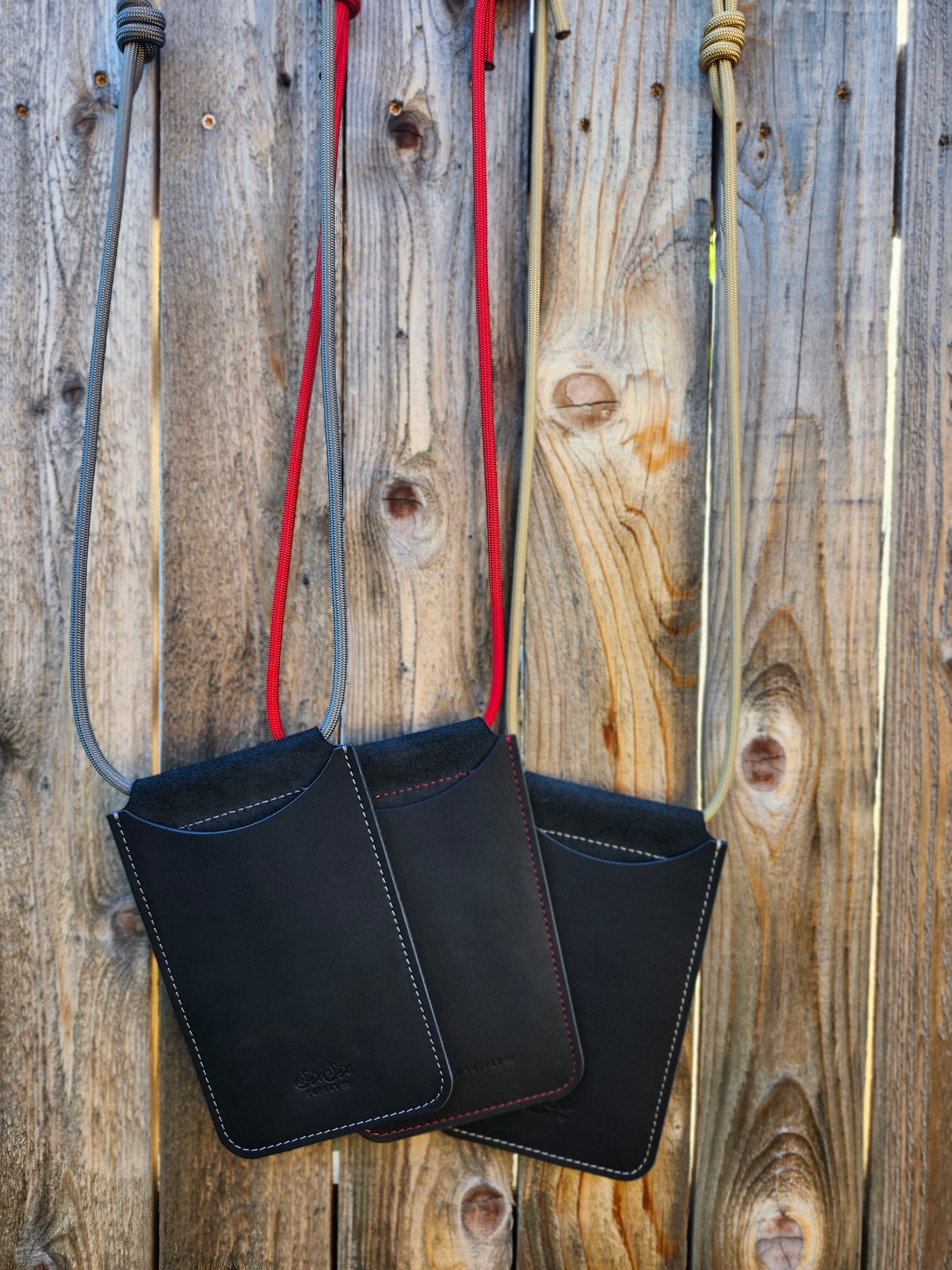 Black leather phone pockets with a silver, red, and gold strap on a wooden surface